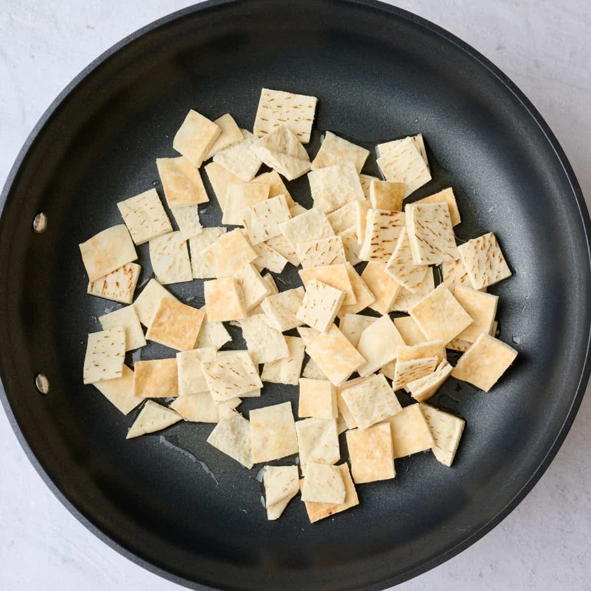 Pita bread pieces in the same skillet before toasting.