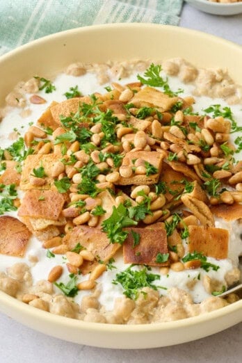 Bowl of chickpea fatteh made with mashed chickpeas, yogurt sauce, toasted pita, and pine nutes.