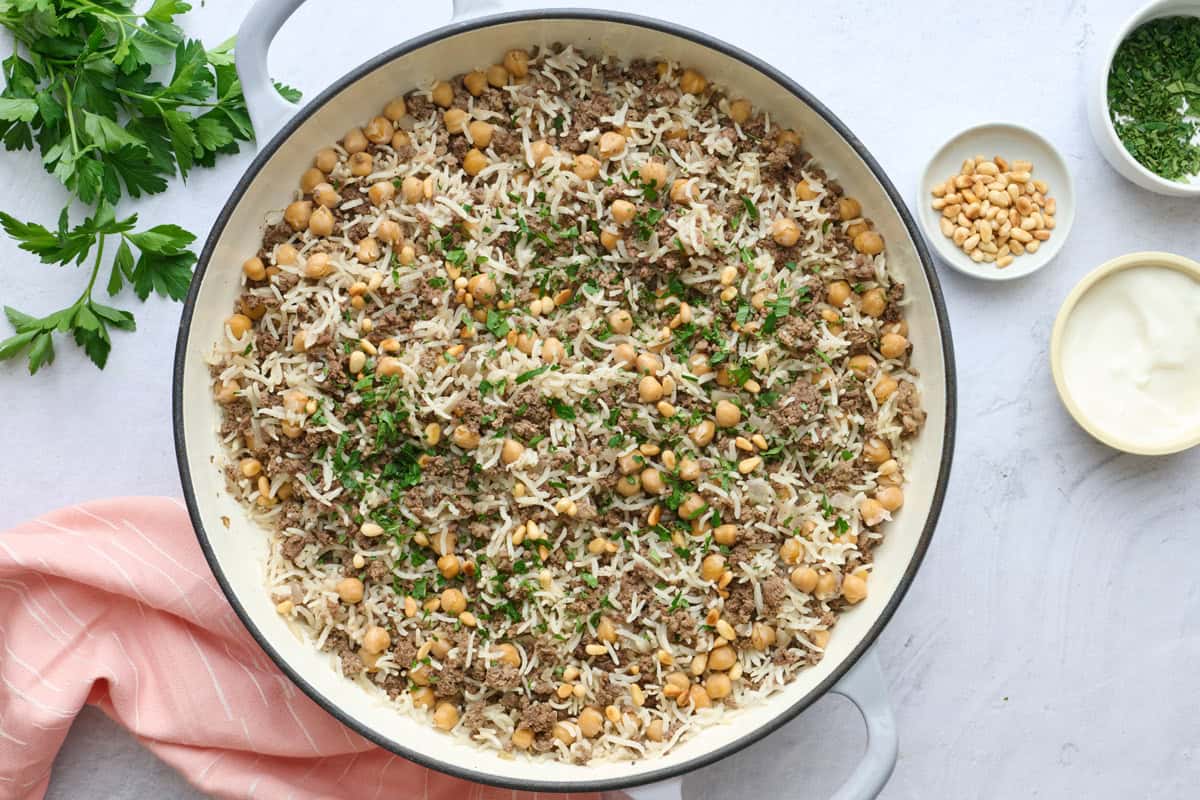 One pan ground beef and rice recipe garnished with chopped parsley and toasted pine nuts for serving.