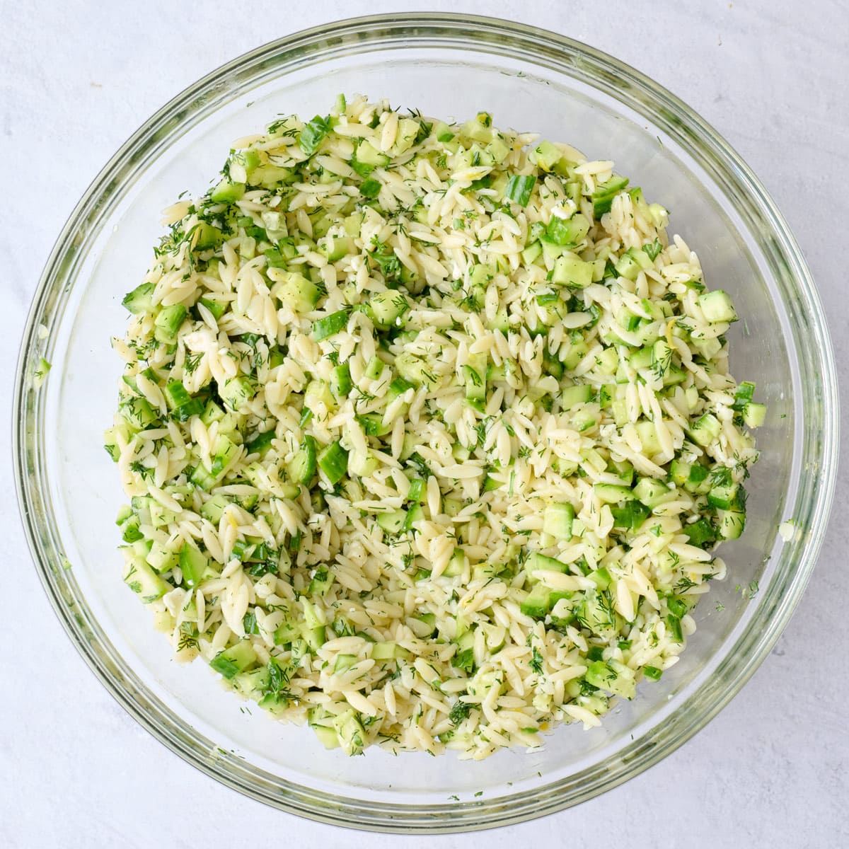 Fresh lemon orzo and cucumber salad in a mixing bowl after tossing together.
