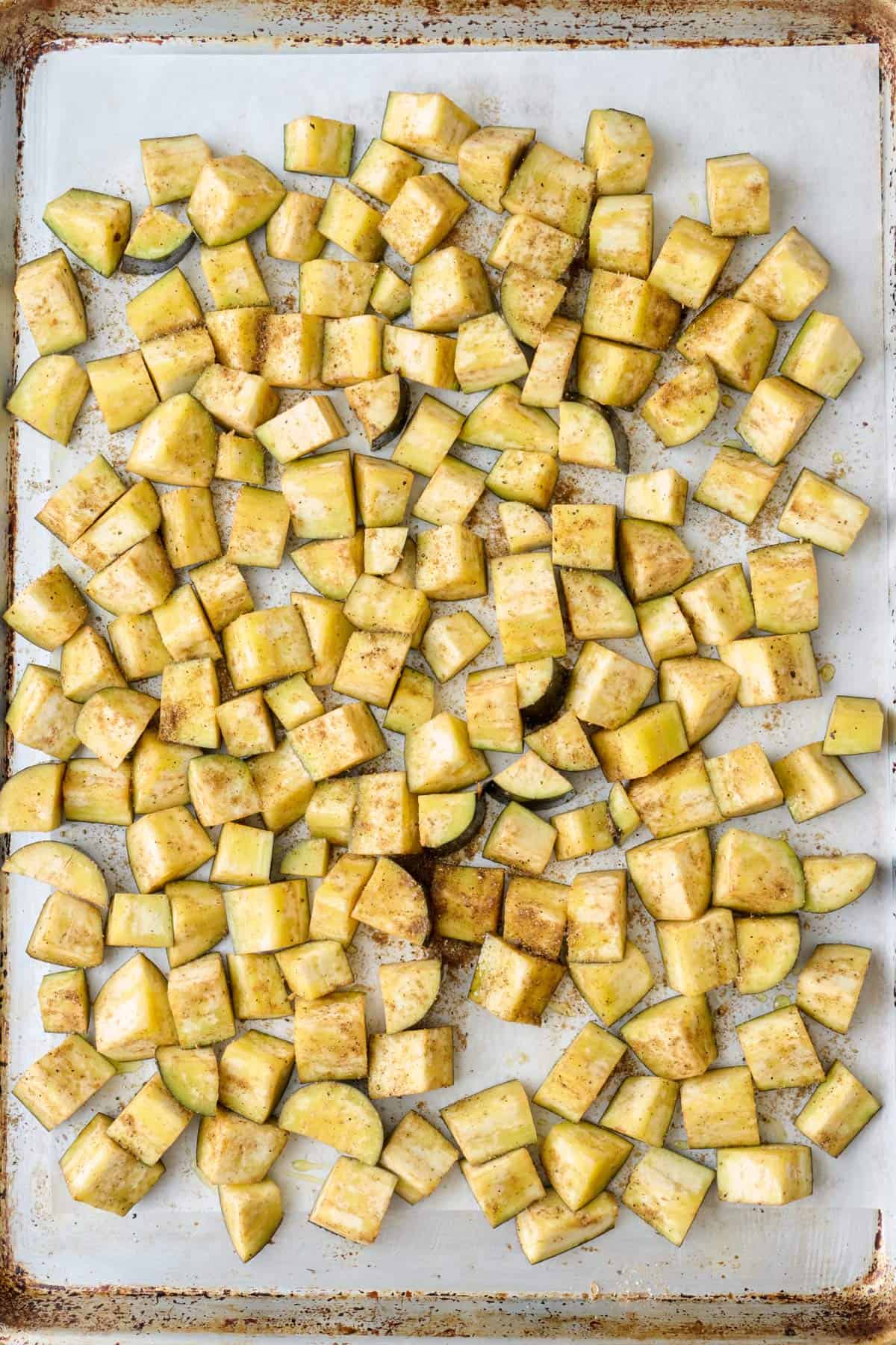 Seasoned eggplant cubes on a baking sheet before roasting.