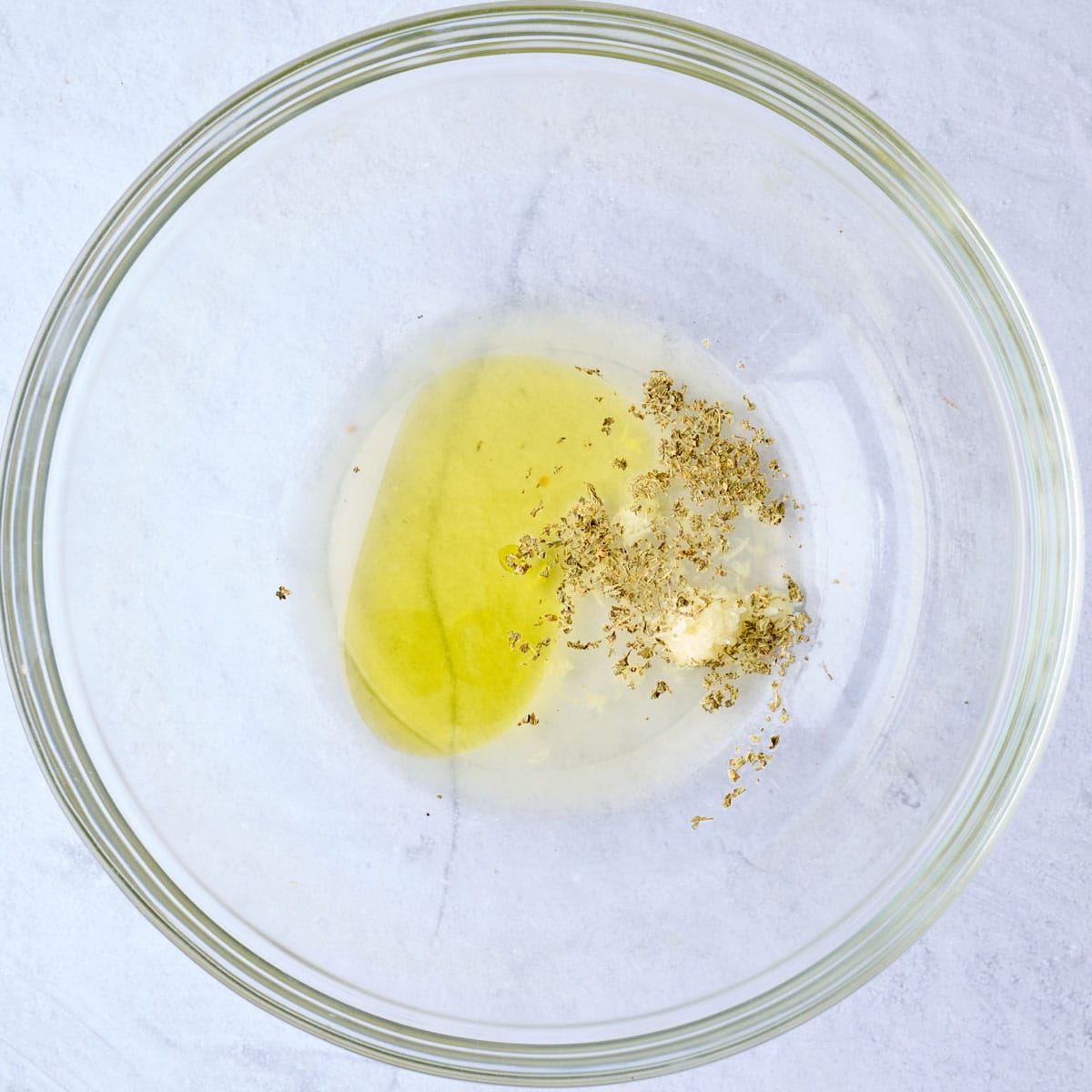 Olive oil, lemon juice, garlic, and oregano in a large bowl before whisking.