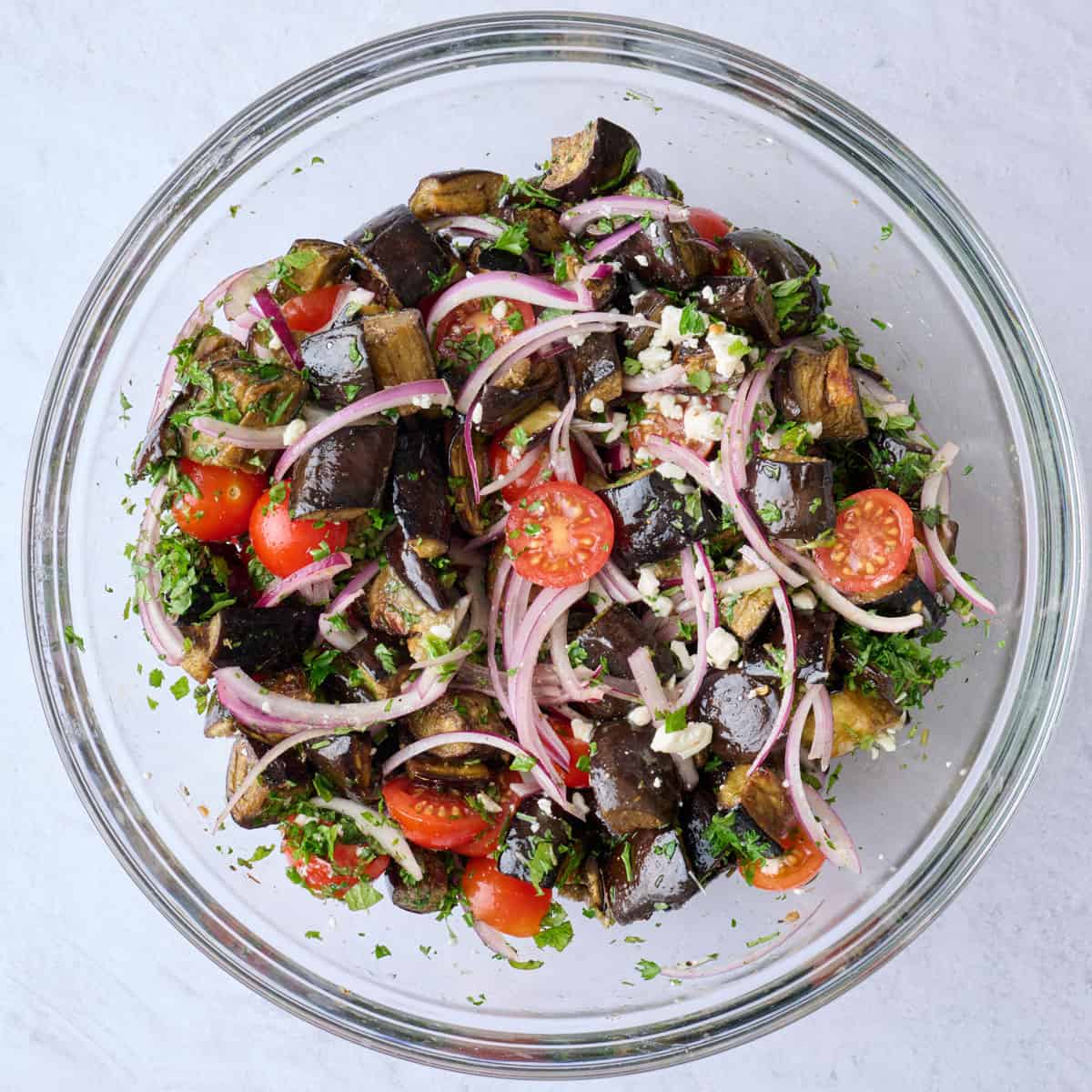 Roasted eggplant salad ingredients tossed together with dressing in a bowl.