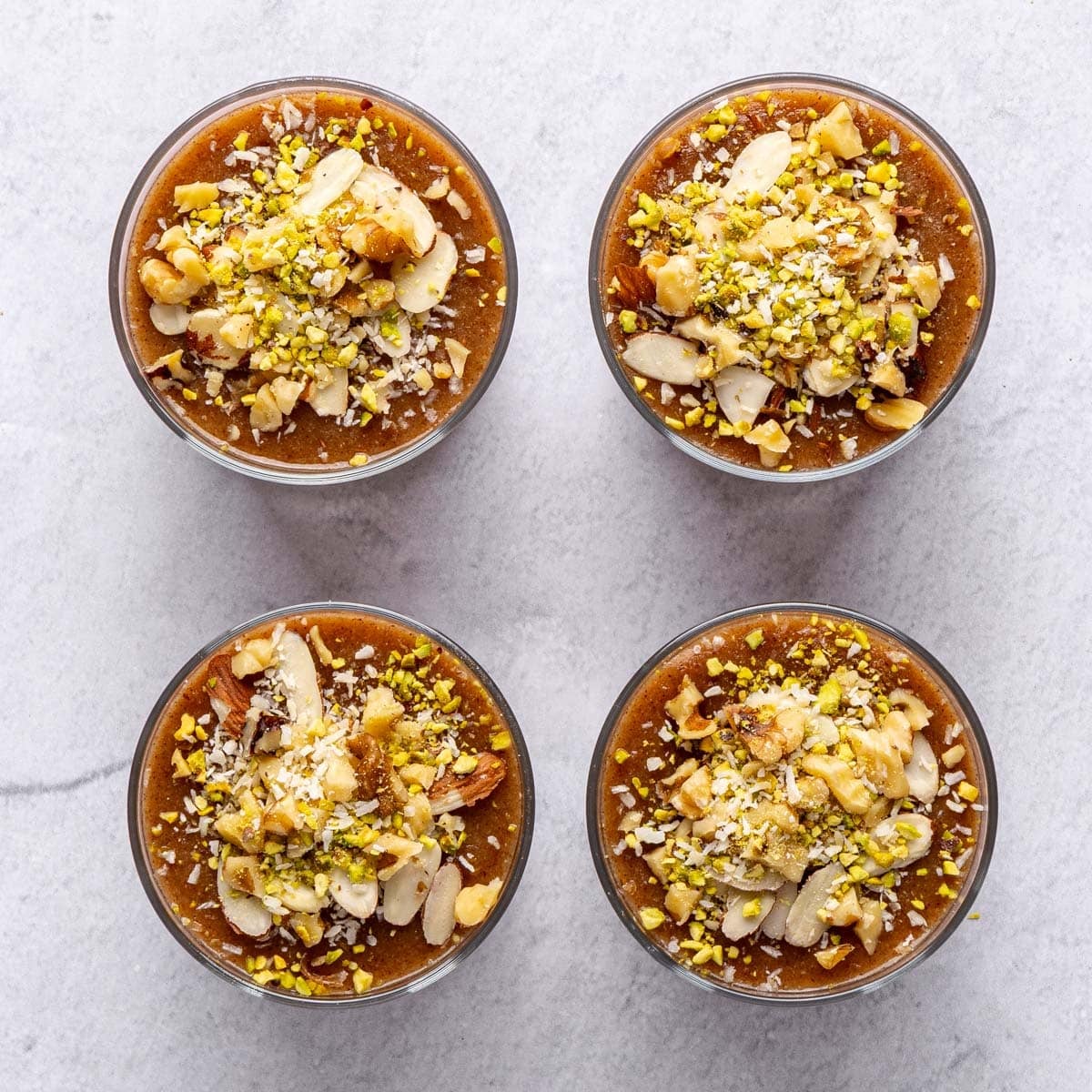 Four dessert cups filled garnished with toppings.