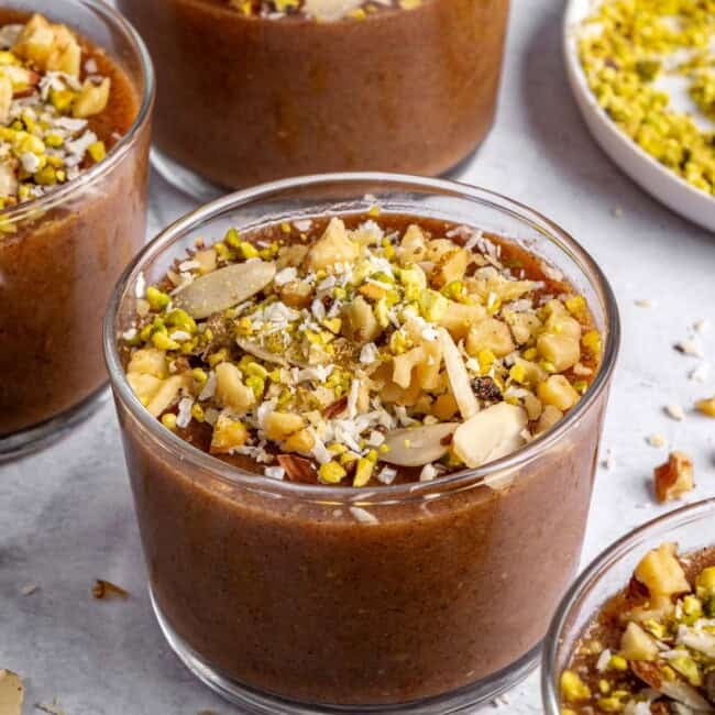 Three dessert bowls of meghli, staggered with extra ingredients around.