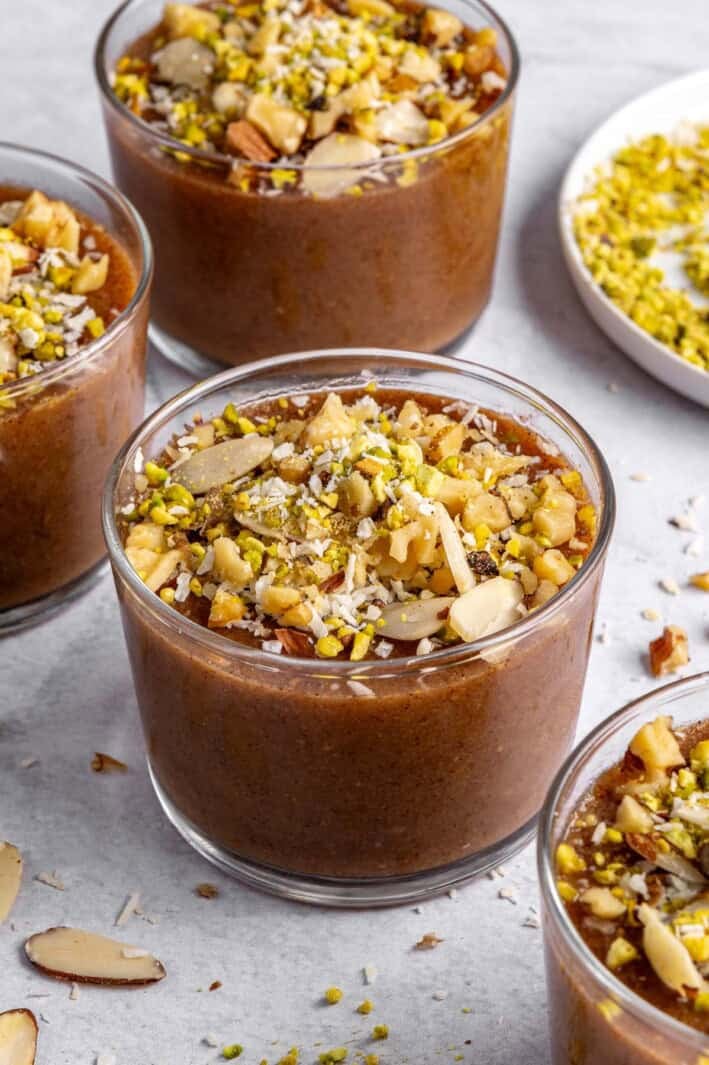 Three dessert bowls of meghli, staggered with extra ingredients around.