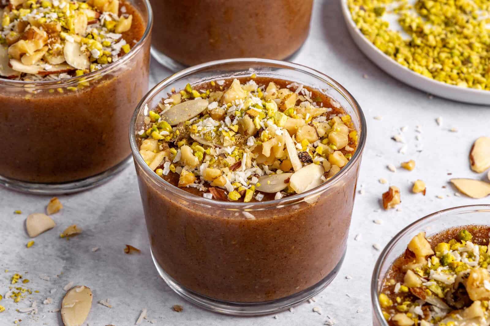 Three dessert bowls of meghli, staggered with extra ingredients around.