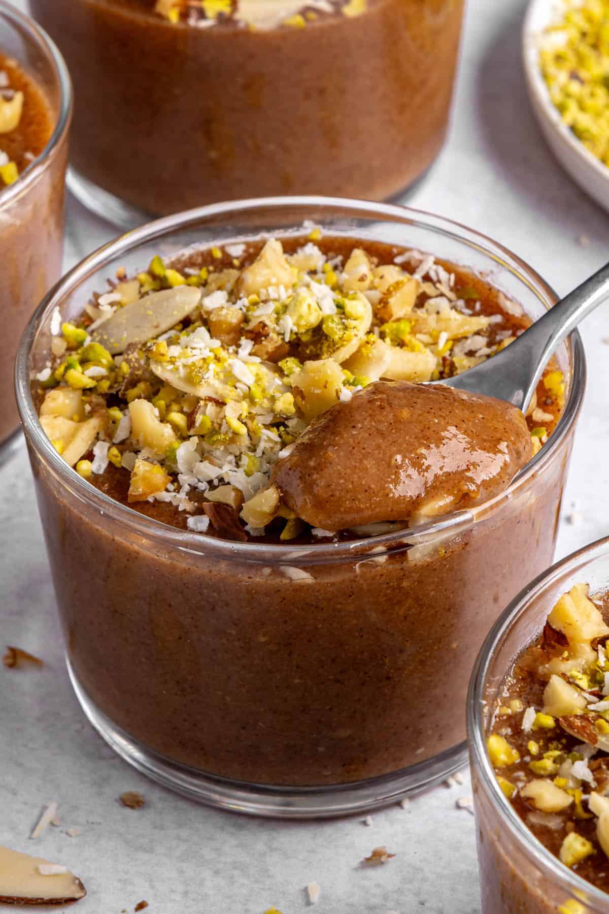 A spoon lifting some meghli from a dessert bowl, with other dessert bowls and toppings around.