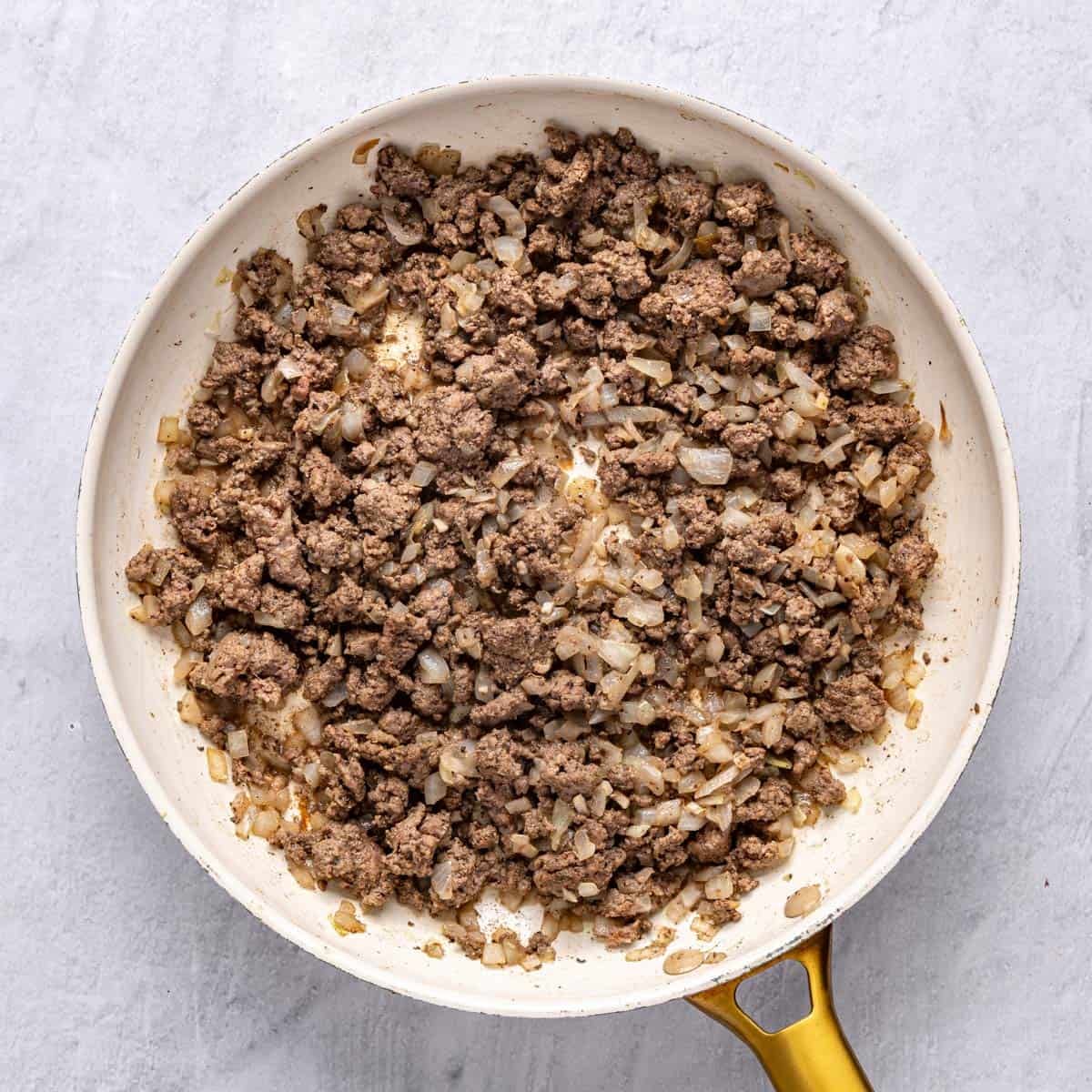 The large skillet filled with cooked beef, onions, garlic, 7 spice, coriander, salt and pepper.
