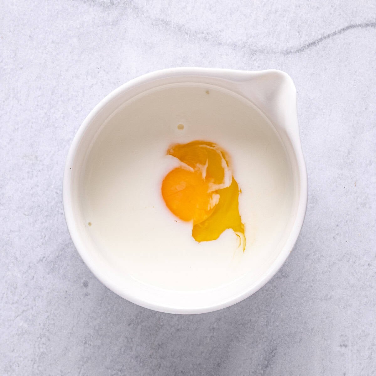 A bowl with egg and milk before whisking them together.
