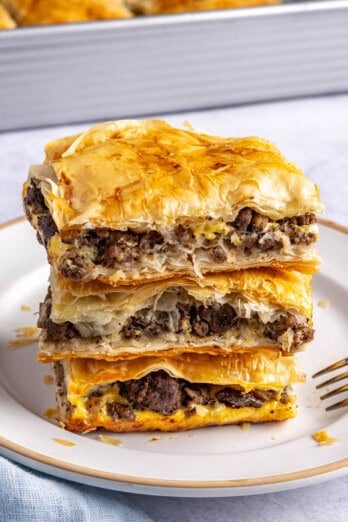 2-3 meat pie squares stacked on a small plate with baking dish in background.