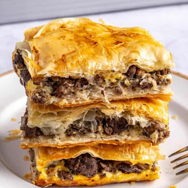 2-3 meat pie squares stacked on a small plate with baking dish in background.