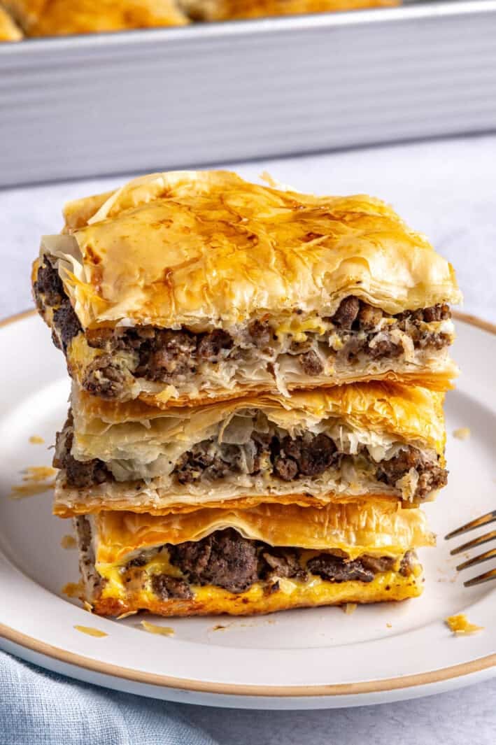 2-3 meat pie squares stacked on a small plate with baking dish in background.