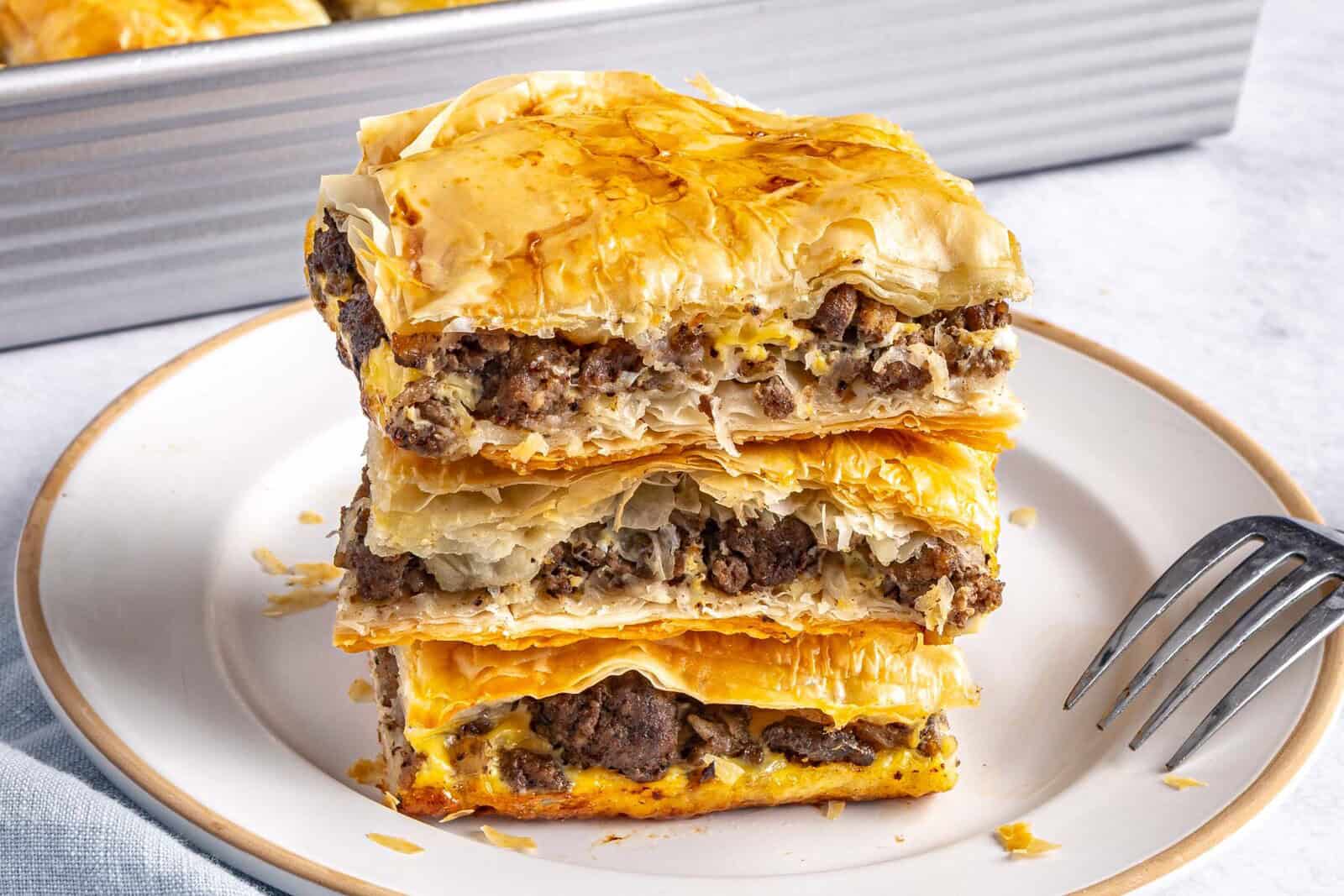 2-3 meat pie squares stacked on a small plate with baking dish in background.