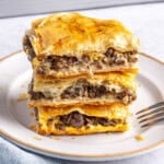 2-3 meat pie squares stacked on a small plate with baking dish in background.