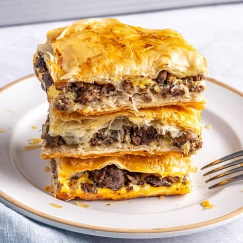 2-3 meat pie squares stacked on a small plate with baking dish in background.