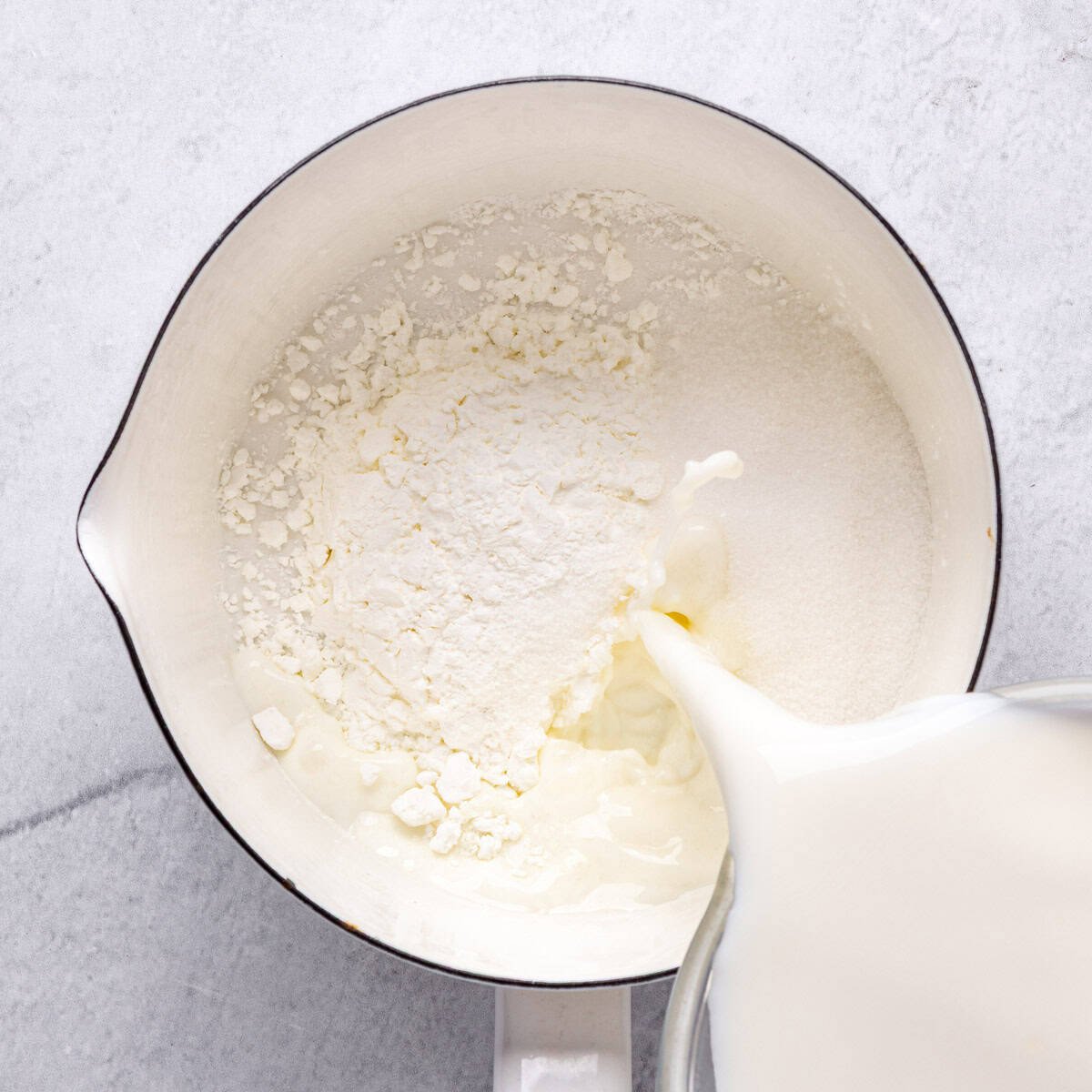 Cornstarch and sugar in a saucepan with milk being poured in.