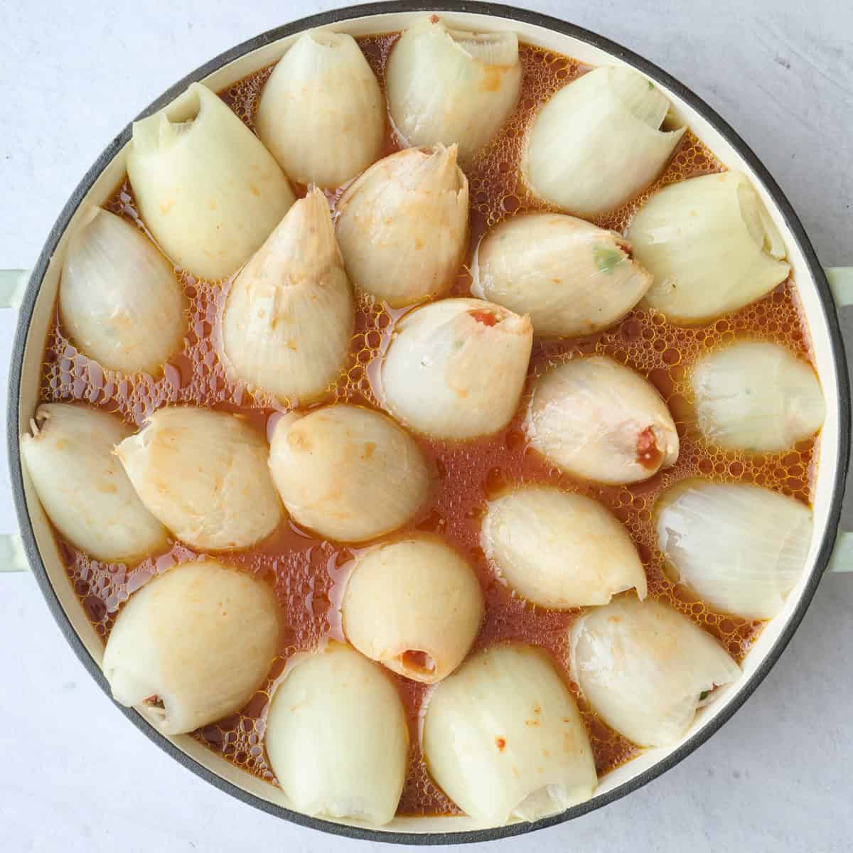 Tomato sauce poured over uncooked stuffed onions before baking.