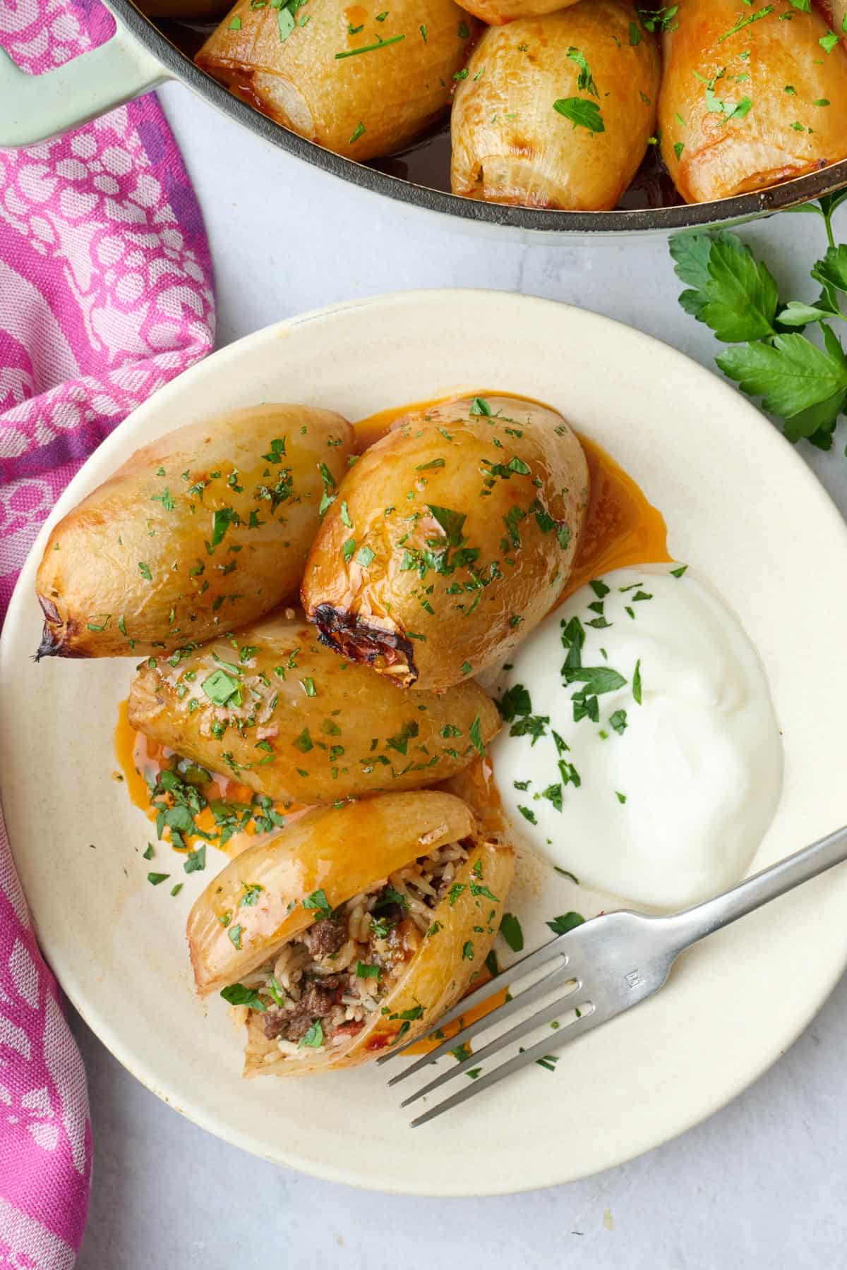 Ground beef rice stuffed onions on a serving plate with one onion cut open to show filling inside, served with yogurt.