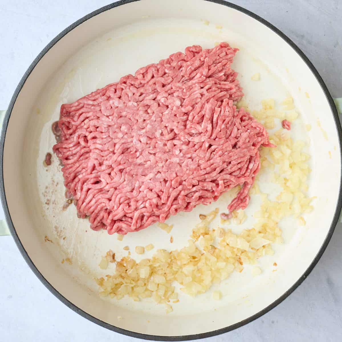 Cooked onions in a skillet with ground beef added.