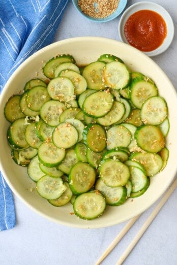 Asian cucumber salad in a serving bowl with sesame seeds sprinkled on top, small dishes of extra sesame seeds and chopsticks nearby.