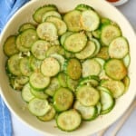 Asian cucumber salad in a serving bowl with sesame seeds sprinkled on top, small dishes of extra sesame seeds and chopsticks nearby.