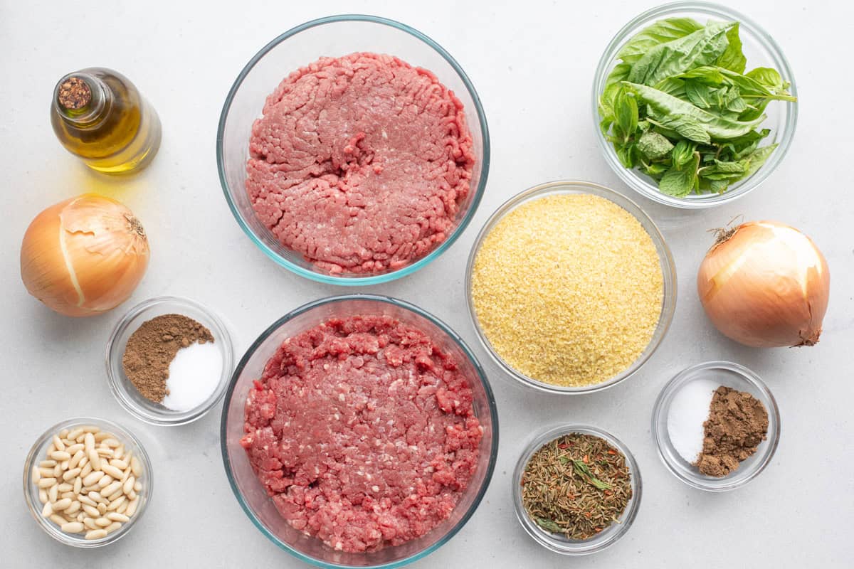 Ingredients for kibbeh recipe before prepping: oil, onion, 7 spice, salt, pine nuts, bulgur wheat, fresh basil, kamouneh spice, and ground beef.