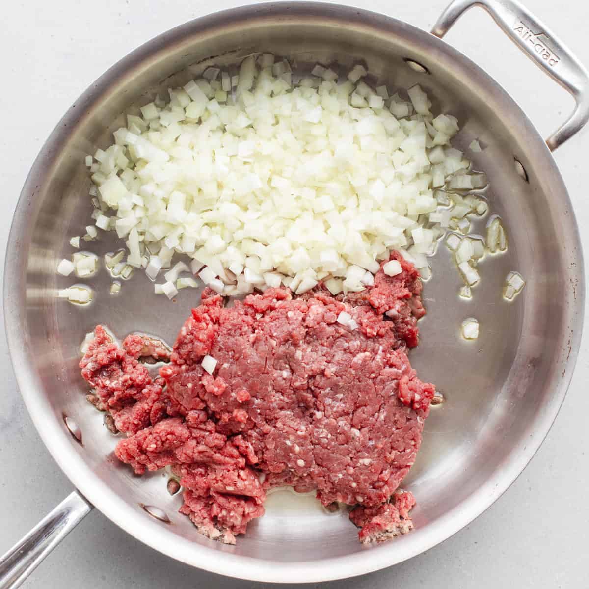 Ground beef and onions in a pan before cooking.