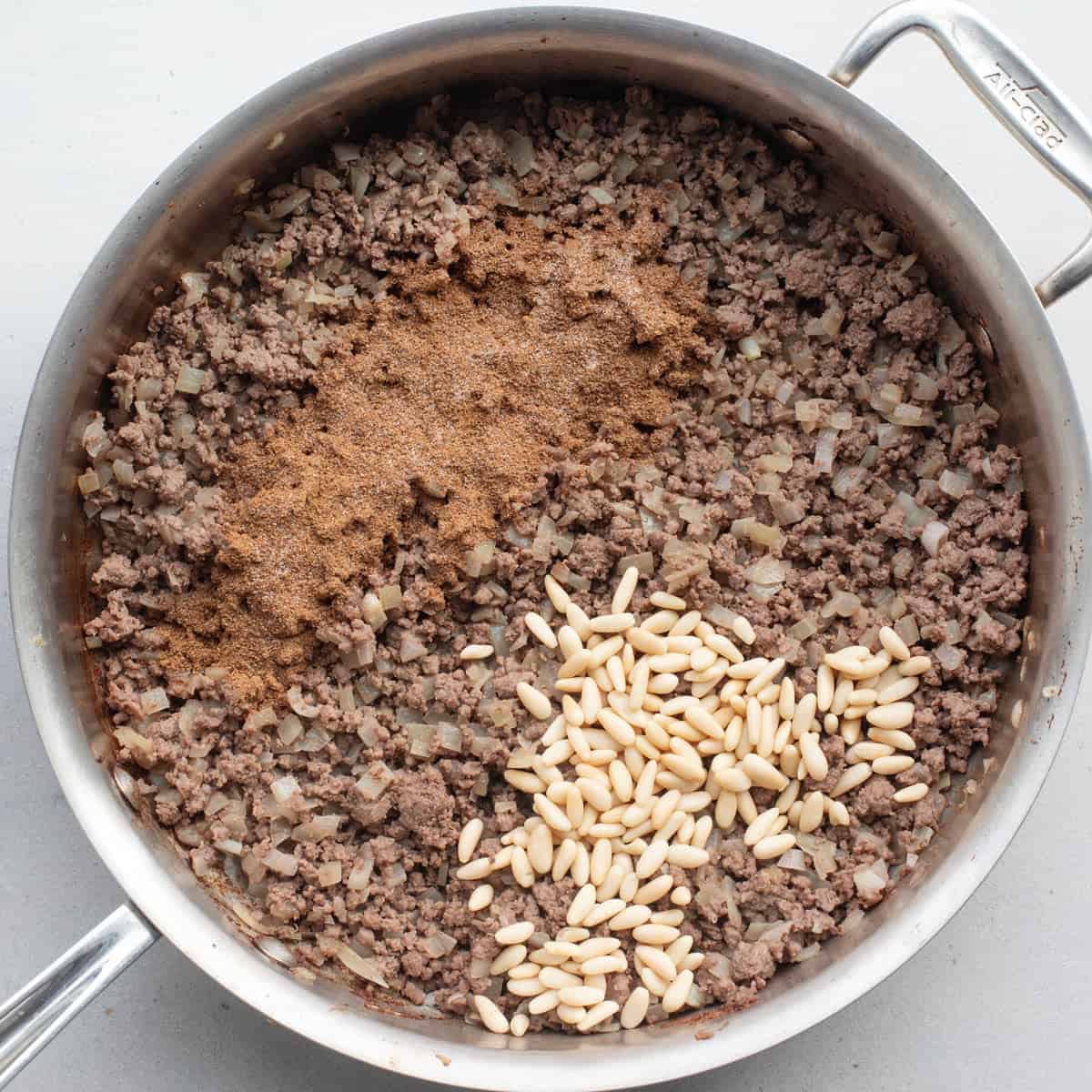 Ground beef and onions after cooking with spices and pine nuts added before combining.