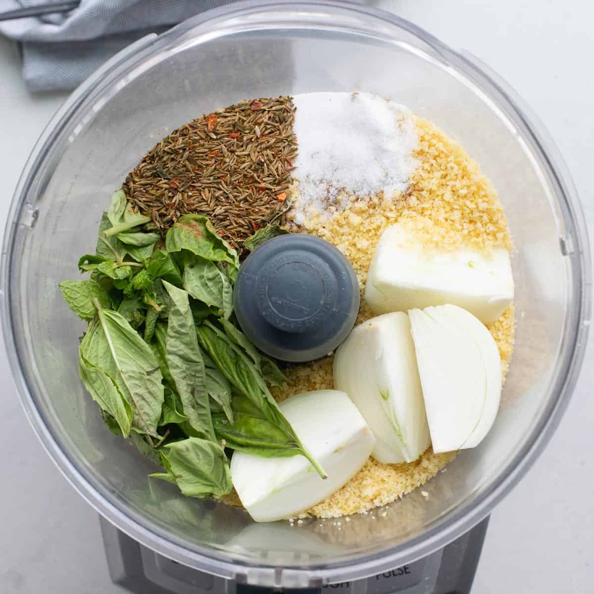 Bulgur, spices, herbs, and onions added to a food processor before processing.