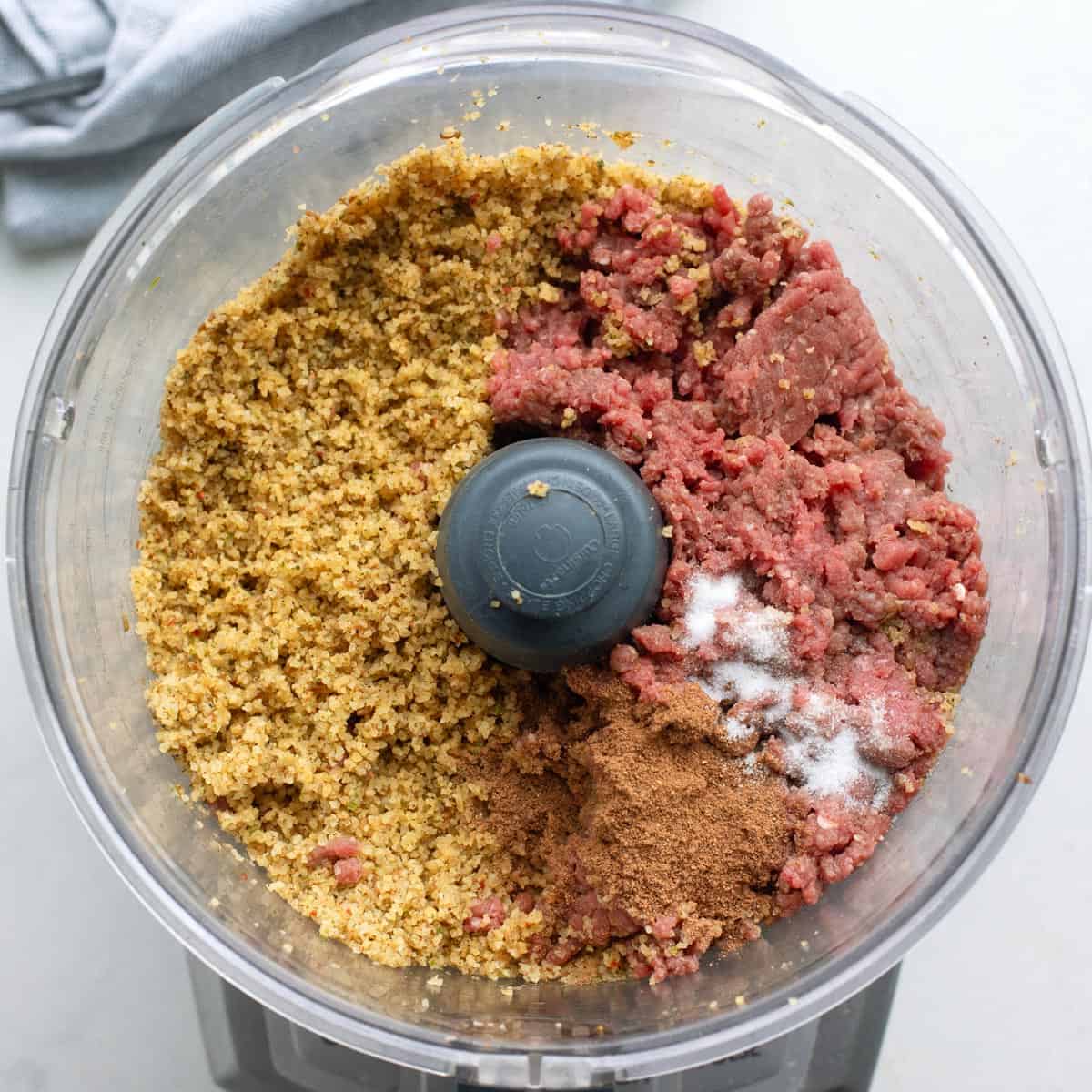 Ground beef and spices added to bulgur mixture in a food processor before mixing.