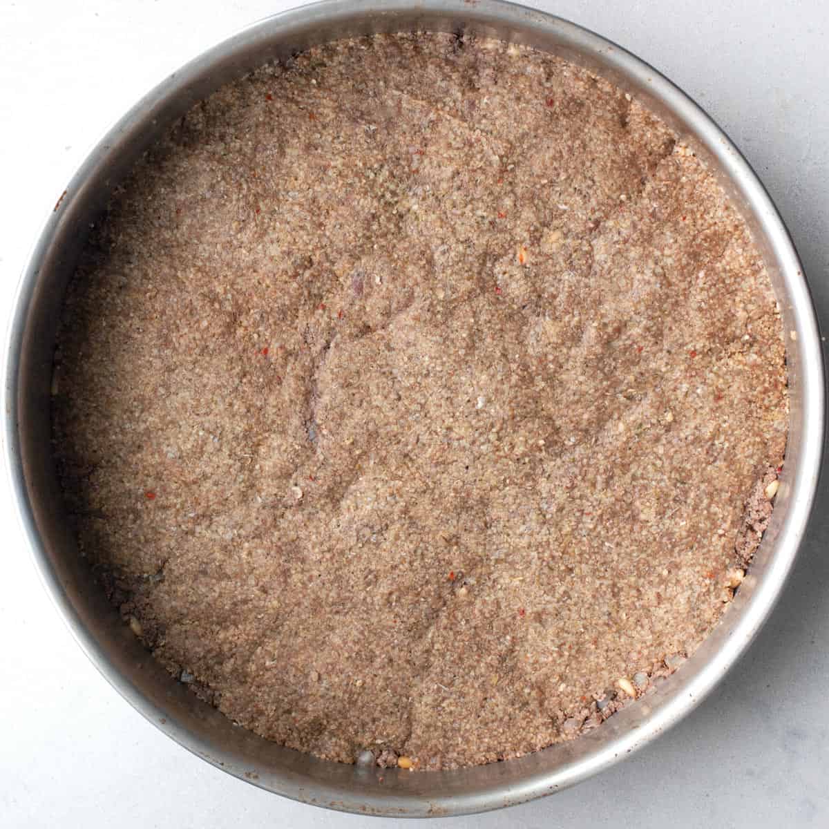 After pressing the ground meat and spiced bulgur mixture into a round pan before baking.