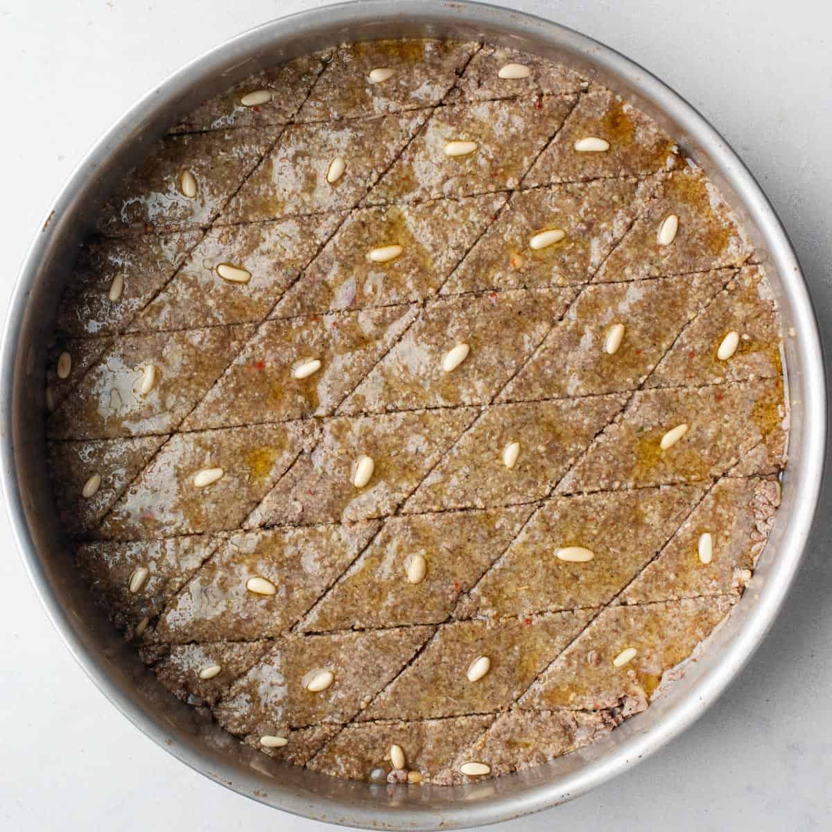 After slicing unbaked kibbeh mixture into small diamonds then topped with pine and oil.