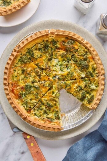 Broccoli cheese quiche cut into 8 slices, one slice removed to plate nearby.