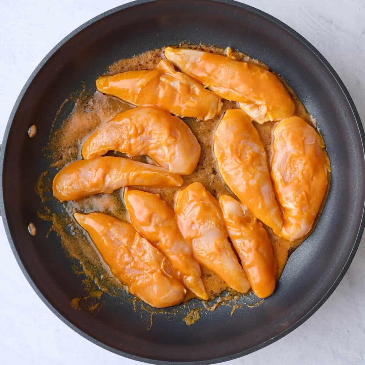 Marinated tenders in a large skillet before cooking.