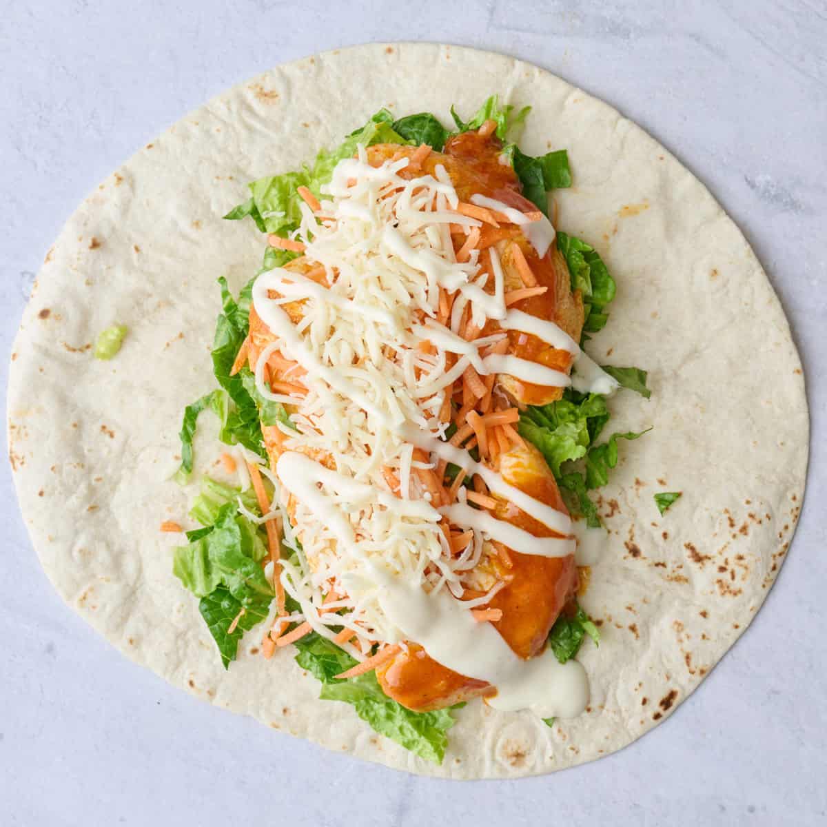 Wrap on surface with romaine, cheese, carrots, buffalo chicken with any extra sauce and ranch drizzled on top.