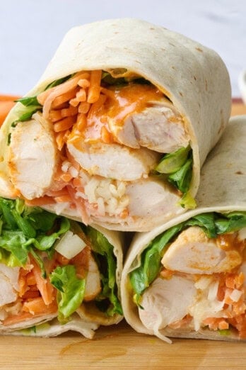 Buffalo chicken wraps after assembling with two cut in half with cut side facing forward, side of carrots and celery in background