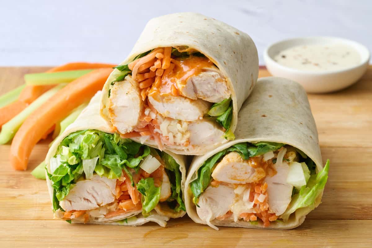 Buffalo chicken wraps after assembling with two cut in half with cut side facing forward, side of carrots and celery in background