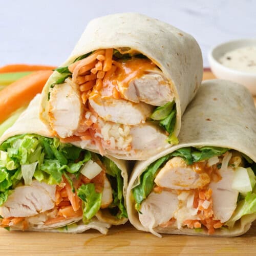 Buffalo chicken wraps after assembling with two cut in half with cut side facing forward, side of carrots and celery in background