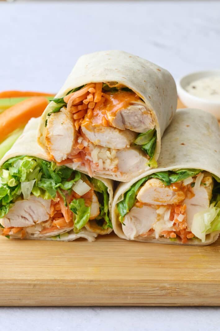 Buffalo chicken wraps after assembling with two cut in half with cut side facing forward, side of carrots and celery in background