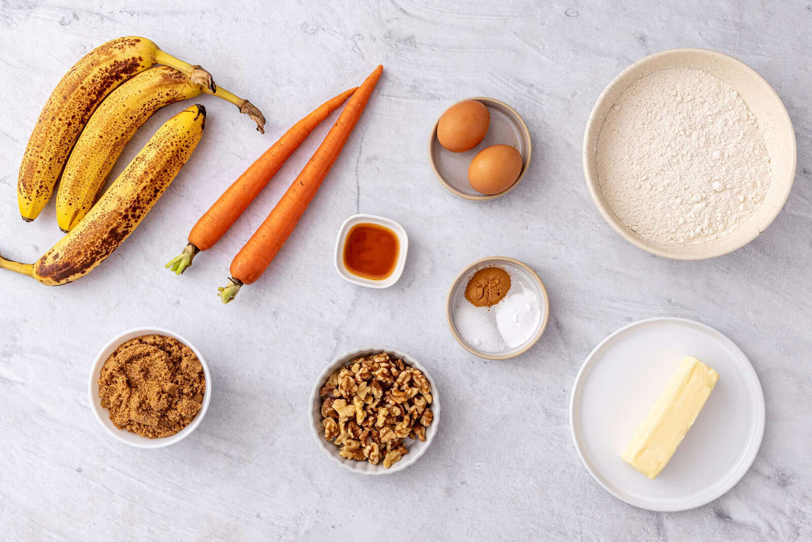 Ingredients for carrot banana bread recipe: ripe bananas, carrots, vanilla, brown sugar, walnuts, eggs, butter, flour, salt, baking powder, and cinnamon.
