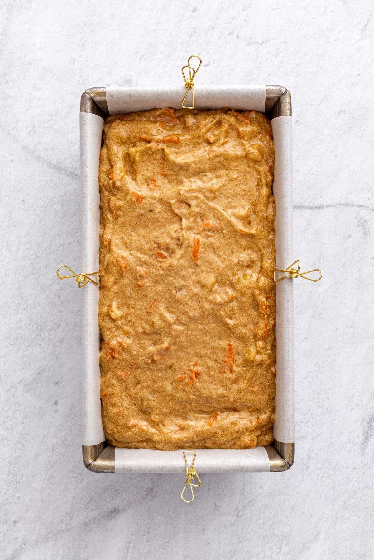Carrot banana bread batter in a parchment line loaf pan before baking.