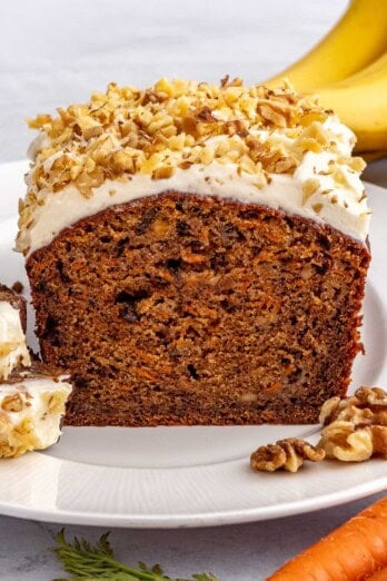 Best carrot banana bread recipe topped with cream cheese frosting and walnuts on a plate with a slice cut away to show inside texture.