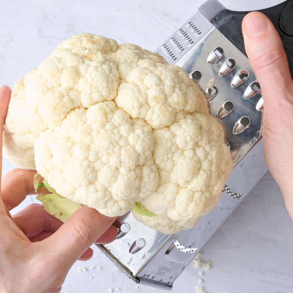 Half a head of cauliflower being grated on using a box grater for salad recipe.