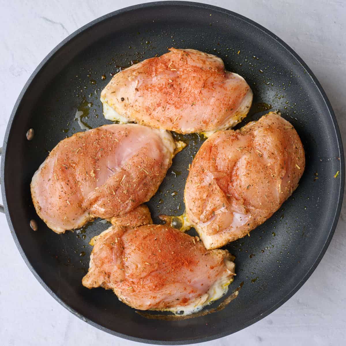 Seasoned chicken breast in skillet before cooking.