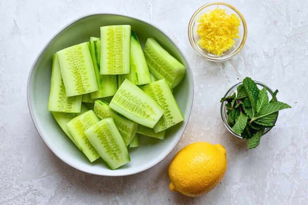 Ingredients for juice recipe: peel and quartered cucumber pieces, lemon, lemon zest, and mint leaves.