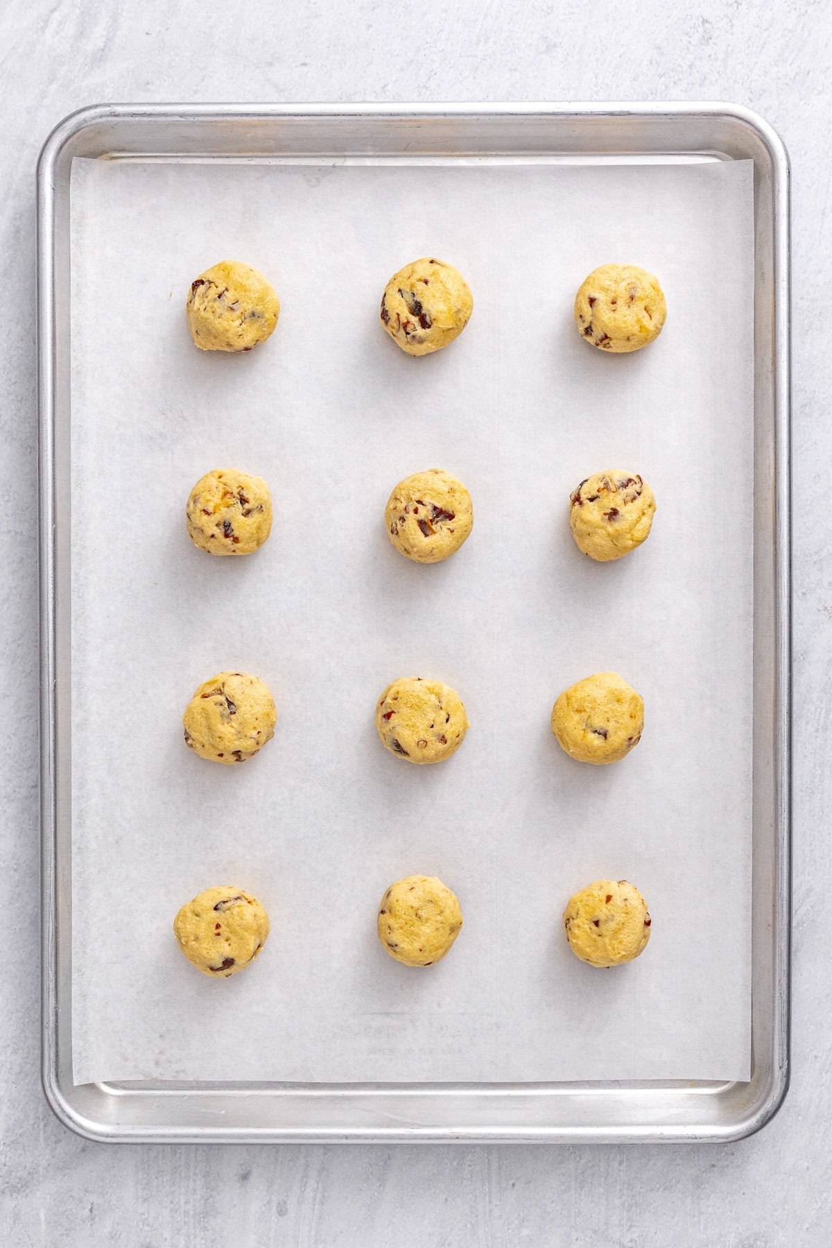 Date cookie dough balls on a parchment lined sheet pan before baking.