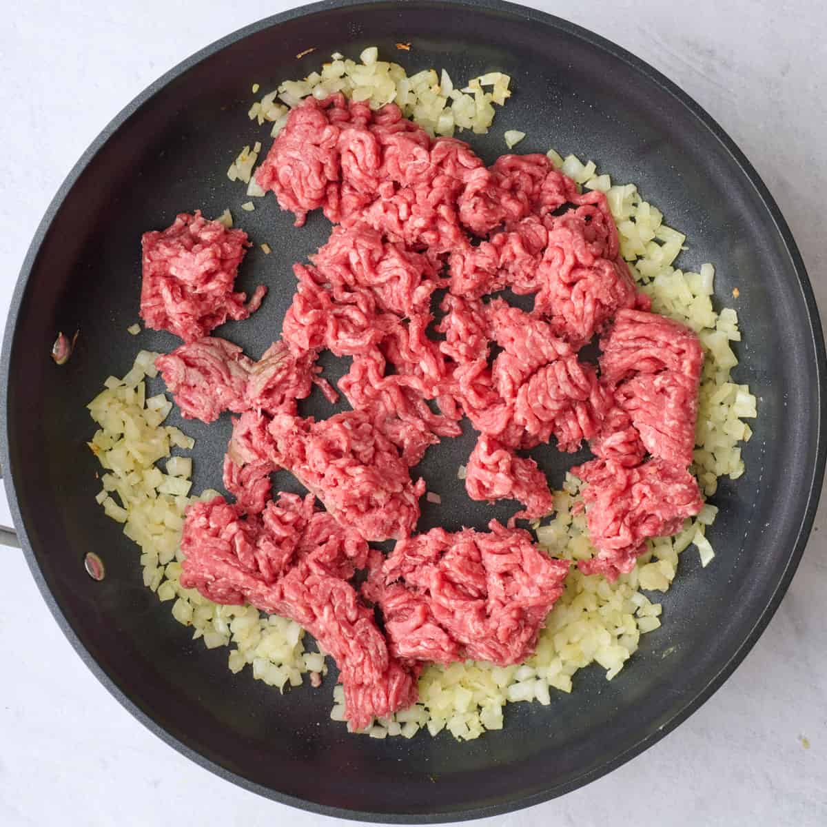 Cooked onions in a large skillet with ground beef added before browning.