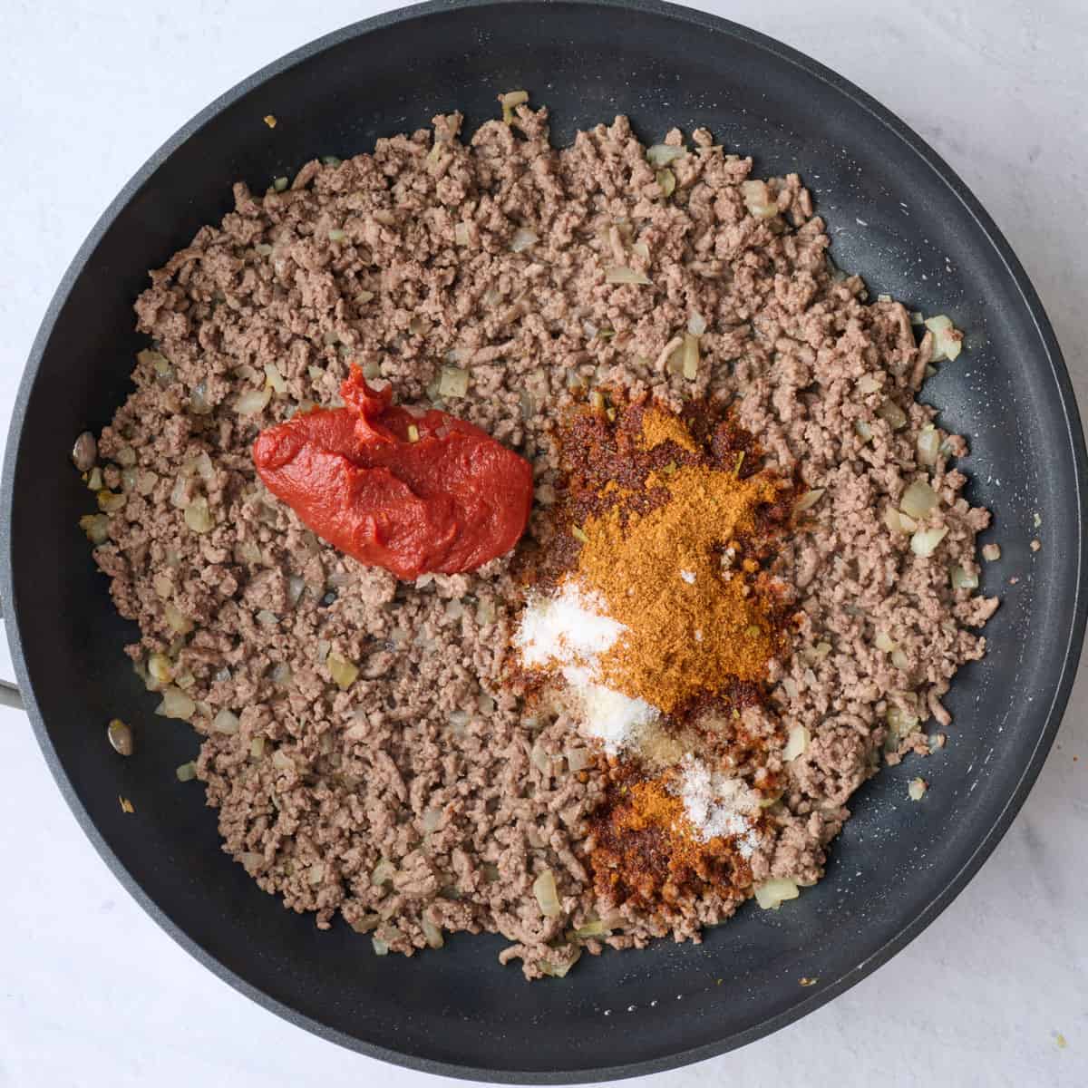 Cooked ground beef and onions with tomato pasta and taco seasonings added before combining.