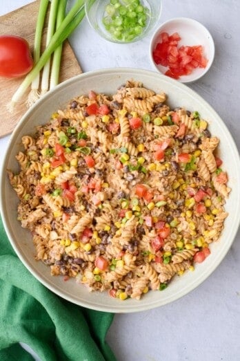 Easy taco pasta salad recipe tossed in a creamy sauce in a serving bowl with corn, beans, cheese, and tomatoes.